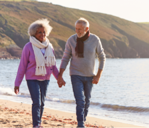 senior couple walking along beach smiling and holding hands