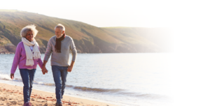 Elderly couple smiling and walking on the beach with sweaters