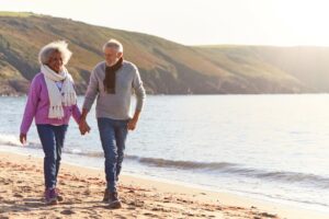 mixed senior couple walking on beach holding hands and smiling