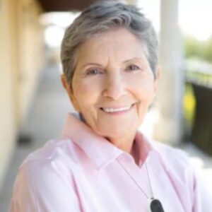 An eldery lady in a pink sweater smiling with a medical alert device around her neck.